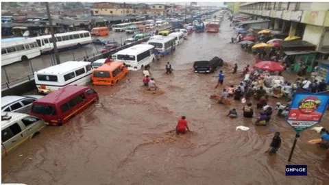 Commuters wading through severe flooding on an Accra street with stranded vehicles